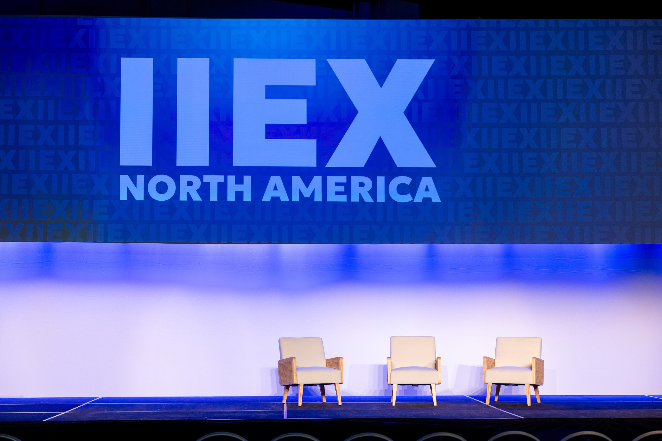 modern, white armchairs on a state in front of a corporate event backdrop that reads IIEX North America